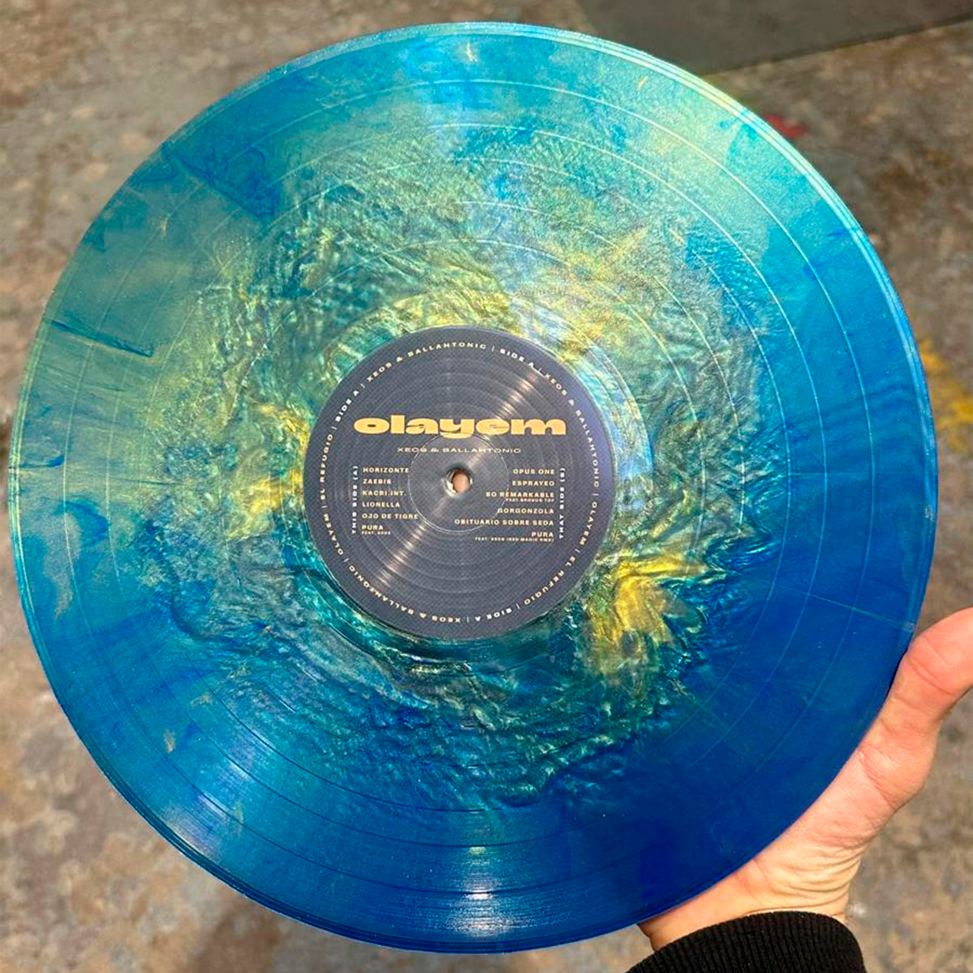 Presentación interna del disco Olayem con el nombre del álbum en el centro y diferentes tonos de amarillo, azul y verde.